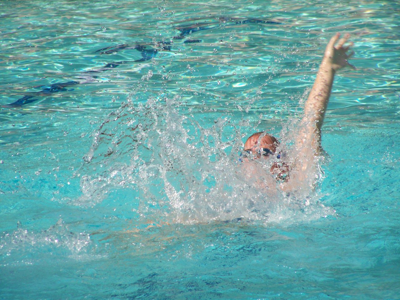 A person swimming in the water with their arms up.
